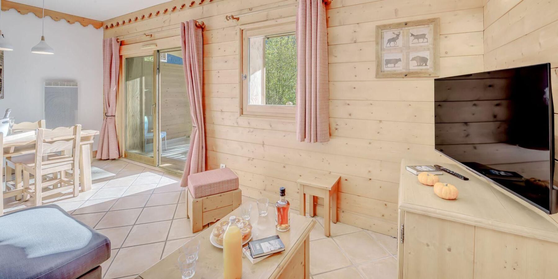 Un interior de madera acogedor con comedor, televisor y ventana con cortinas.