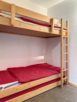 Ein Etagenbett mit einer Leiter, roter Bettwäsche und einer strukturierten Wand.