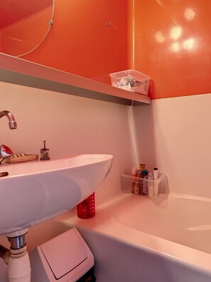 Ein Badezimmer mit einem weißen Waschbecken, einem roten Zahnbürstenhalter und einer weißen Badewanne.