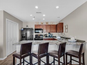 A modern kitchen with granite countertops, stainless steel appliances, wooden cabinets, and a large island with bar stools.