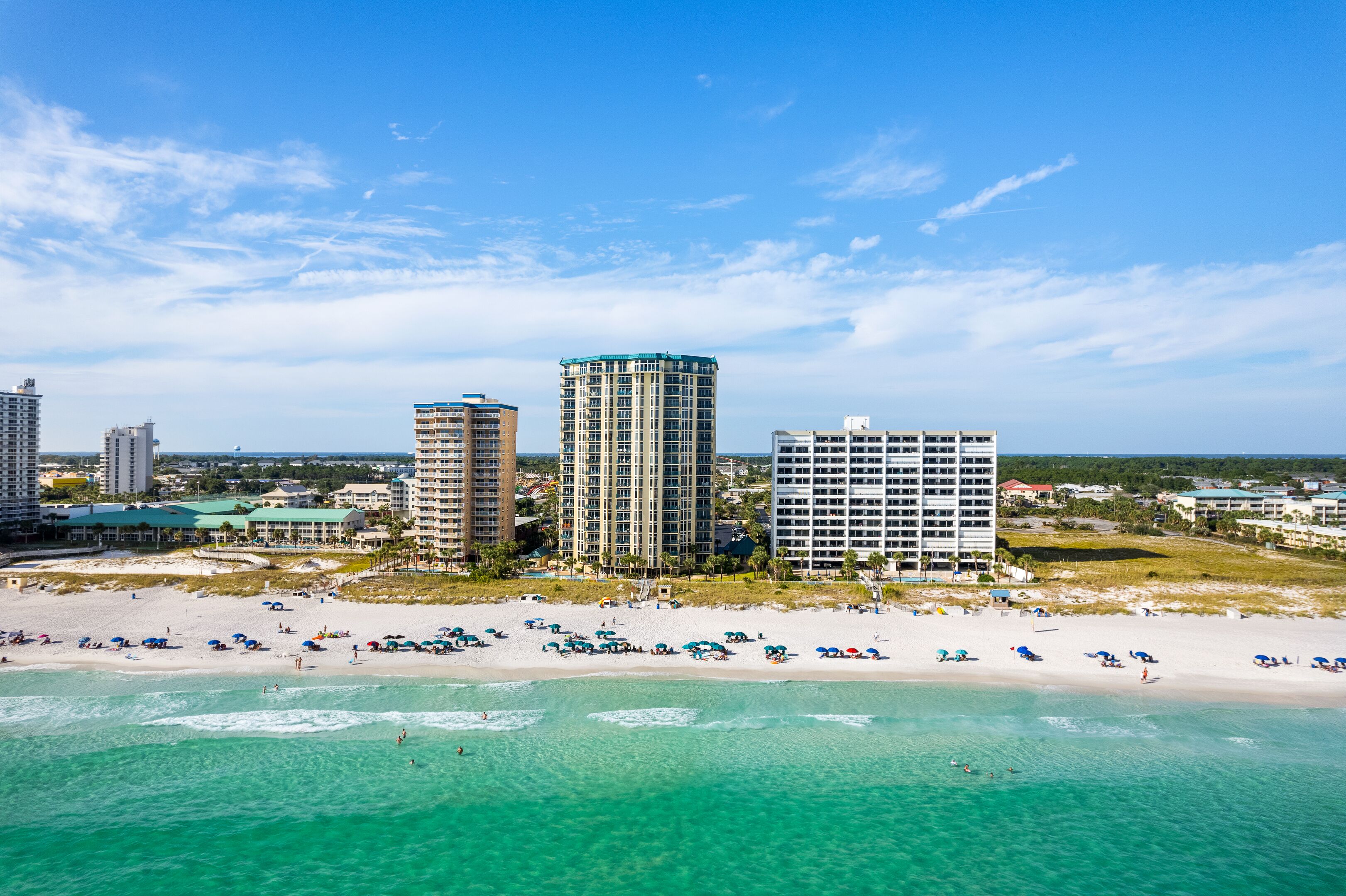 A beachside hotel with multiple high-rise buildings, a sandy beach with umbrellas, and clear turquoise waters.