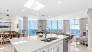 A spacious kitchen with a large island, a dining area with wooden chairs, and a view of the ocean through large windows. - Spectacular Beachfront Penthouse at Jade East Towers (Destin)