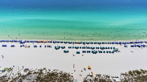 A beach with rows of blue umbrellas and beach chairs, a sandy shore, and the ocean in the background. - Spectacular Beachfront Penthouse at Jade East Towers (Destin)