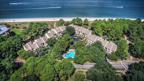 Vista aerea di un resort costiero con piscina circondata da alberi, spiaggia e cielo sereno.
