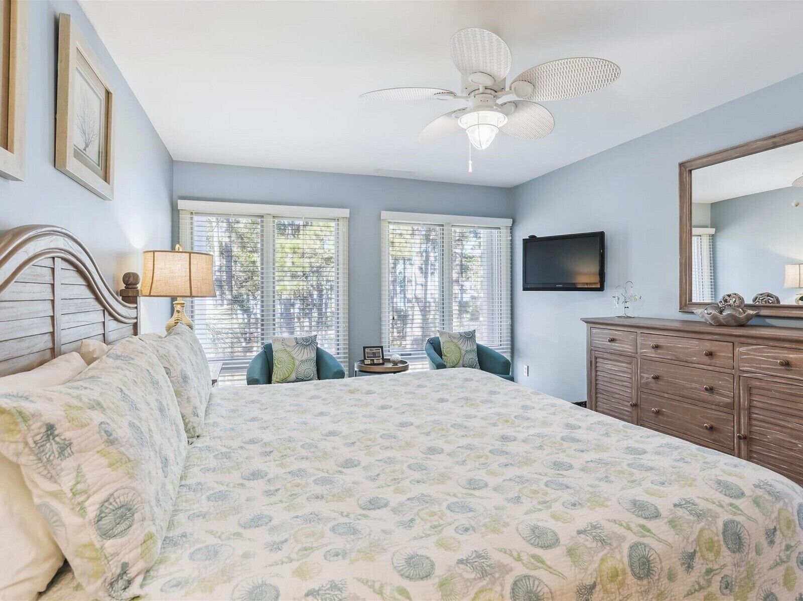 Une chambre avec un grand lit, un ventilateur de plafond, une commode et un téléviseur fixé au mur.