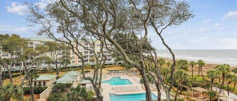 A resort with a pool, palm trees, and a view of the ocean.