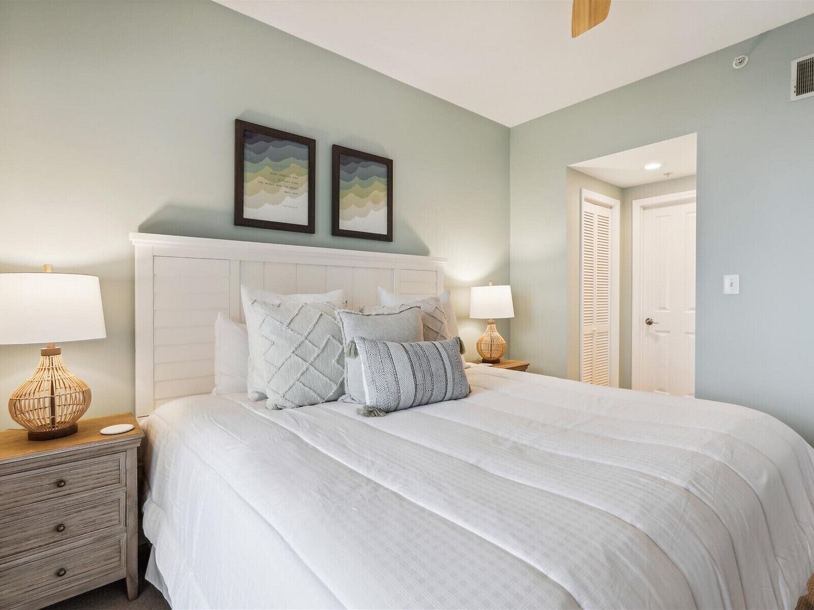 A bedroom with a large bed, two bedside tables, a white headboard, and two framed pictures on the wall.