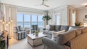A spacious living room with a large window offering a view of the ocean, a ceiling fan, and a modern coffee table. - Direct Ocean Front Views from the 4th Floor (Hilton Head Island)