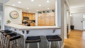 A modern kitchen with a central island, bar stools, wooden cabinets, a microwave, and a clock on the wall. - Direct Ocean Front Views from the 4th Floor (Hilton Head Island)