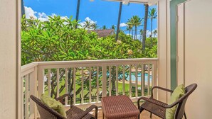 Un balcon agrémenté de meubles en osier, offrant une vue sur une piscine et une végétation tropicale.