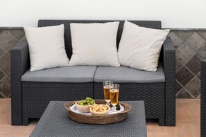A wicker sofa with grey cushions, a tray with snacks and drinks, and a tiled floor.