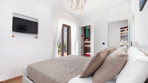 Ein Schlafzimmer mit Bett, Fernseher, einer Kristallleuchtre und einem begehbaren Kleiderschrank.