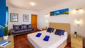 A bedroom with a bed, a sofa, a nightstand, and a wall-mounted lamp.