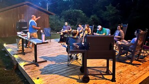 An outdoor gathering with a wooden deck, a barbecue grill, and people seated on chairs. - Cozy and centrally located in the middle of all the best of nature’s offerings!  (Fifty-Six)