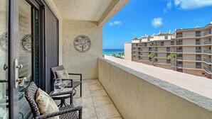 Un balcón con mobiliario de mimbre y vistas al océano y edificios.