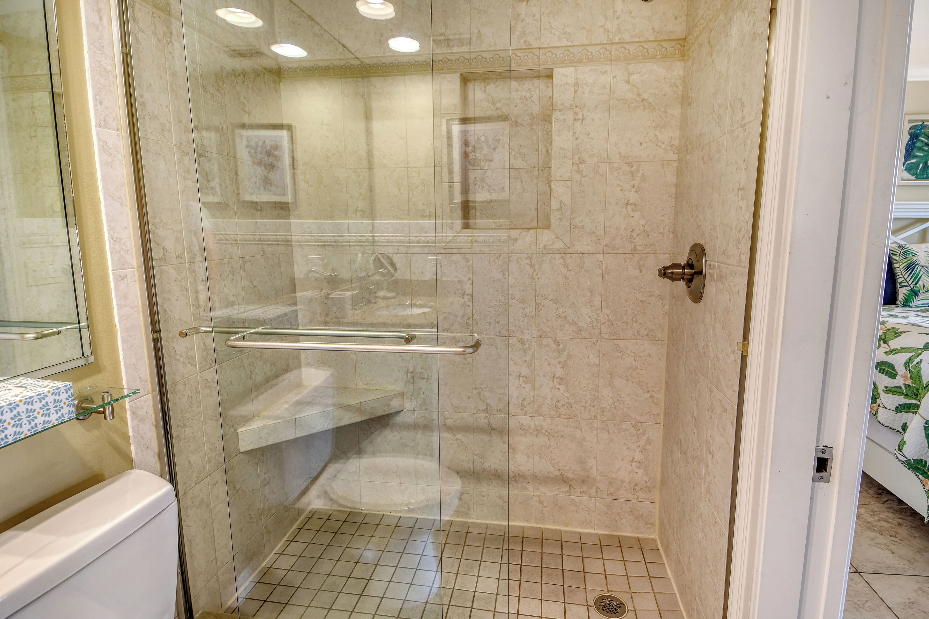 Une douche fermée par des parois de verre avec une porte en verre, des toilettes blanches et une étagère en verre.