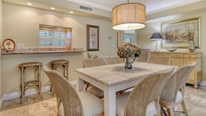 Un comedor con una mesa grande, sillas de mimbre, una lámpara colgante y un jarrón decorativo.