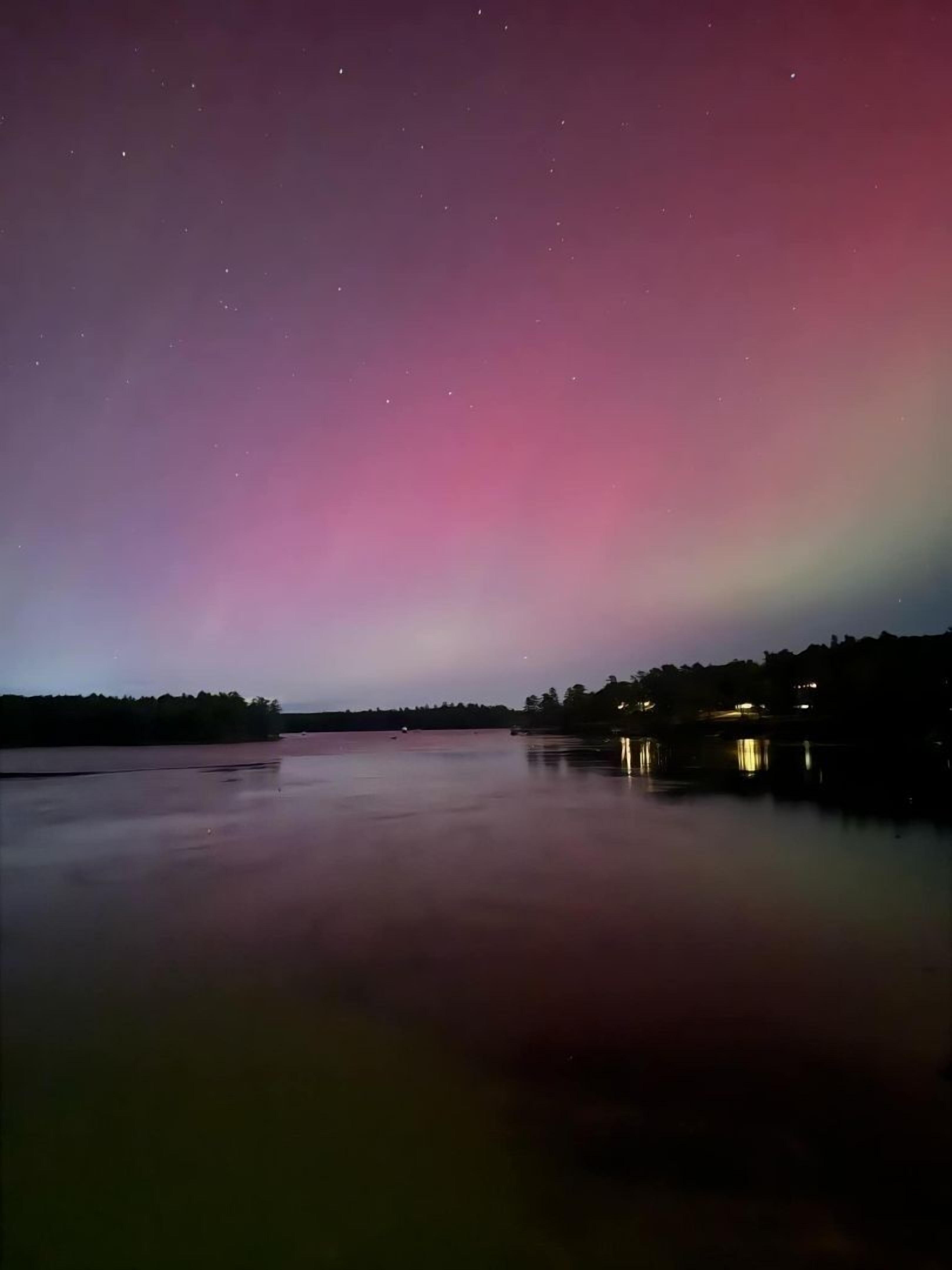A nighttime view of a calm lake with a colorful aurora display in the sky.