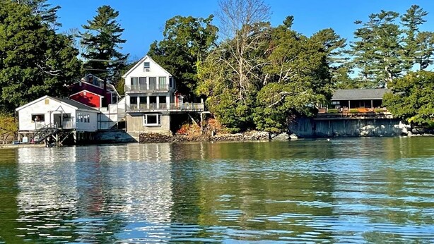 A waterfront property with multiple buildings, including a main house with a balcony and a smaller structure. - Beautiful Oceanfront House- Stunning Water Views (Harpswell)