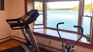 A home gym with a treadmill and elliptical, large windows with a view of a lake and sailboats. - Beautiful Oceanfront House- Stunning Water Views (Harpswell)