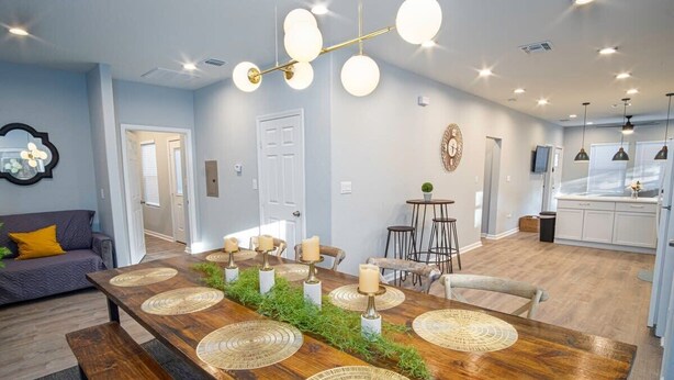A modern living room with a wooden dining table, benches, and a chandelier. - Don't Miss Dynamic 4BR/2BA Near Jolly Riverwalk (San Antonio)