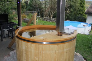 A hot tub with a wooden exterior, a stone wall, and a pool in the background. - Rosebud House. Family vacation home with a large outdoor area (Weilheim)