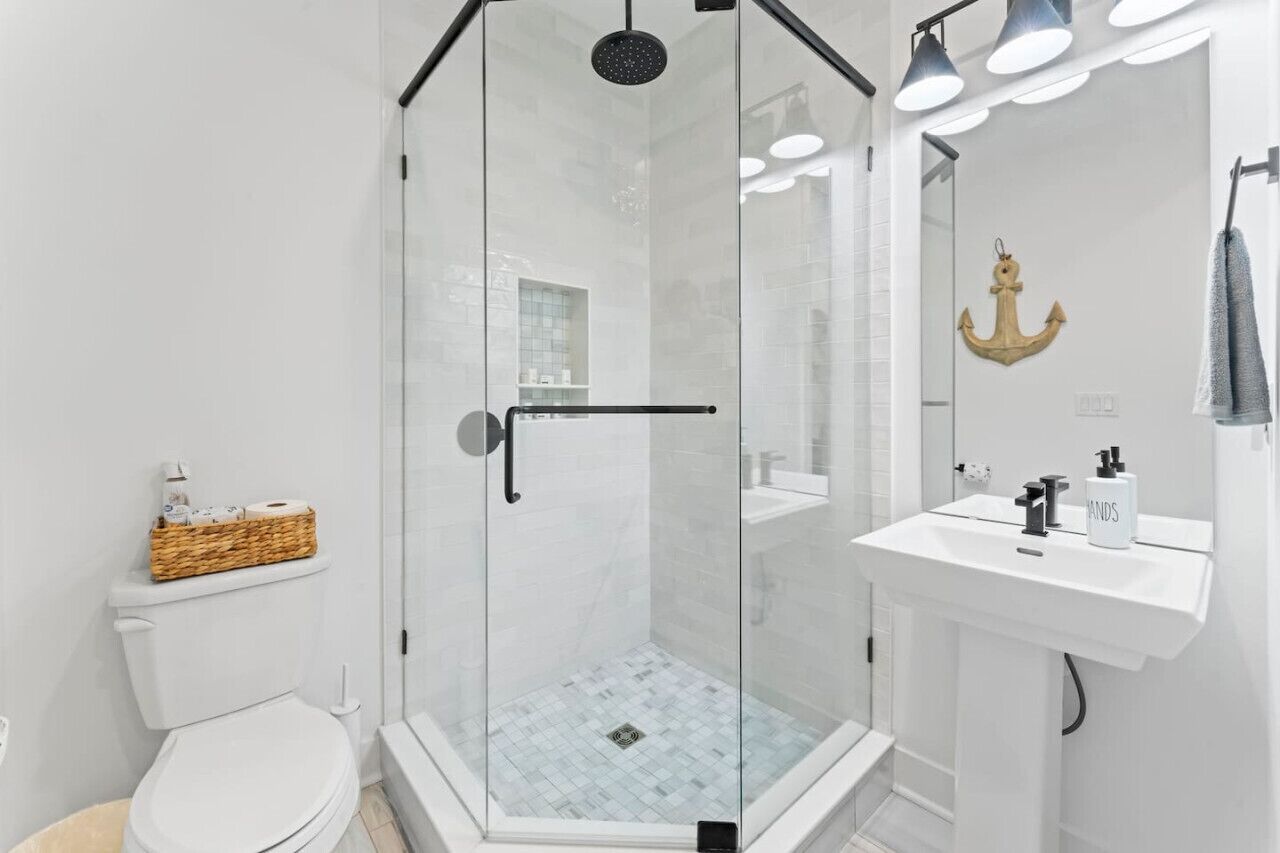 A modern bathroom with a glass-enclosed shower, white fixtures, and a decorative anchor on the wall.