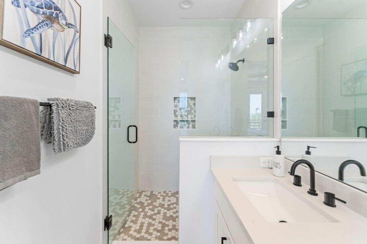 A modern bathroom with a glass shower enclosure, a large mirror, and a white sink with black faucets.