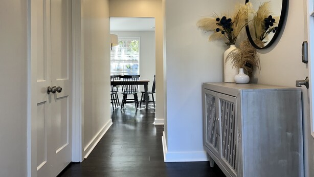 A hallway with a dark wooden floor, white walls, and a dining area in the background. - On-site Laundry, ample and secure parking, Fast Wi-Fi, only 10 mi from 1-95 (Savannah)