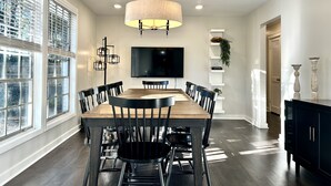 A dining area with a wooden table, black chairs, a chandelier, and a TV on the wall. - On-site Laundry, ample and secure parking, Fast Wi-Fi, only 10 mi from 1-95 (Savannah)