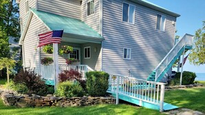 Une maison à deux étages avec des fondations en pierre, un porche doté d’une balustrade blanche et un drapeau américain.