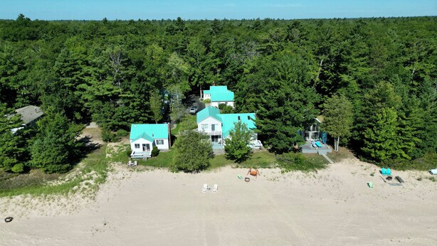 Une propriété située sur la côte, comprenant plusieurs maisons, une plage de sable et une forêt dense en arrière-plan.