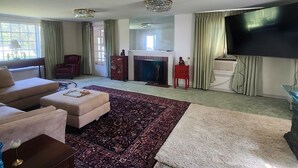 A spacious living room with a large flat-screen TV, a fireplace, and a chandelier.