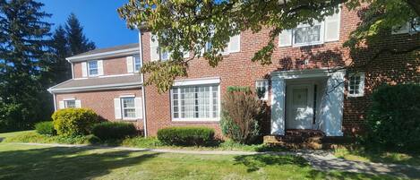 A two-story brick house with a front porch, a large window, and a well-maintained lawn.