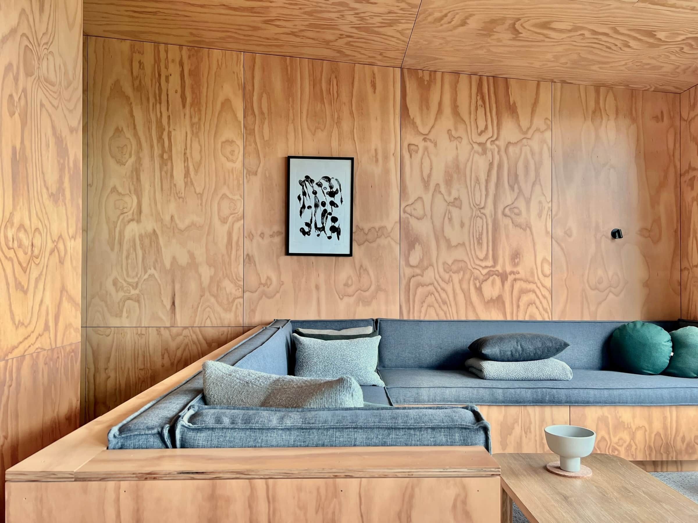 Un salon moderne avec un mur recouvert de panneaux de bois, un canapé gris agrémenté de coussins et une table basse en bois.