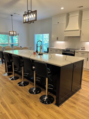A modern kitchen with a large island, bar stools, and a pendant light. - Experience Lake Tuscaloosa views from your 5-bedroom Northport retreat (Northport)