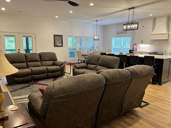 A spacious living area with a brown leather sofa set, a dining table with chairs, and a kitchen with white cabinets and a built-in island. - Experience Lake Tuscaloosa views from your 5-bedroom Northport retreat (Northport)