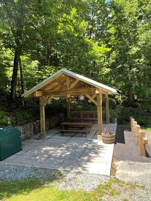 Een houten paviljoen met banken en picknicktafels in een bebost gebied.