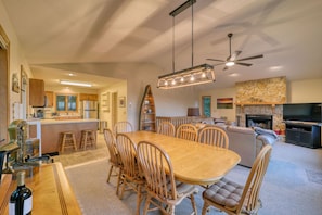 A spacious living area with a dining table, chairs, a fireplace, a TV, and a kitchen in the background.