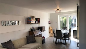 A living room with a sofa, a coffee table, a dining area with chairs and a table, and a bookshelf with books and decorative items. - 3 Bed House - Sleeps 6 - Garden - Parking - Wifi (Rye)