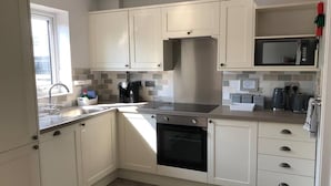 A modern kitchen with white cabinets, a stainless steel range hood, a microwave, and a coffee maker. - 3 Bed House - Sleeps 6 - Garden - Parking - Wifi (Rye)