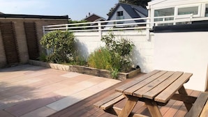A wooden deck with a picnic table, surrounded by a low white wall and potted plants. - 3 Bed House - Sleeps 6 - Garden - Parking - Wifi (Rye)