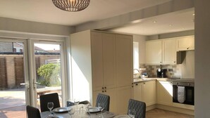 A modern kitchen with white cabinets, a dining area with a table set for six, and a view of the outside. - 3 Bed House - Sleeps 6 - Garden - Parking - Wifi (Rye)