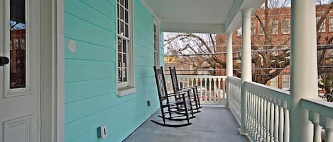 A turquoise house with a porch featuring rocking chairs and a white railing.