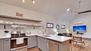 A modern kitchen with stainless steel appliances, a dining area with a TV, and a ceiling fan. - The Ashley Suite (Charleston)