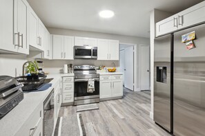 A modern kitchen with white cabinets, stainless steel appliances, and a wooden floor. - Wonderful 3bdr cottage, 5mins from beach (Jupiter)