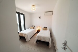 Een kleine, schone kamer met twee eenpersoonsbedden, een nachtkastje met lamp en een raam met zonwering.