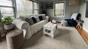 Un salon chaleureux avec un canapé blanc, des coussins à motifs, une table basse rustique et un pouf en osier.