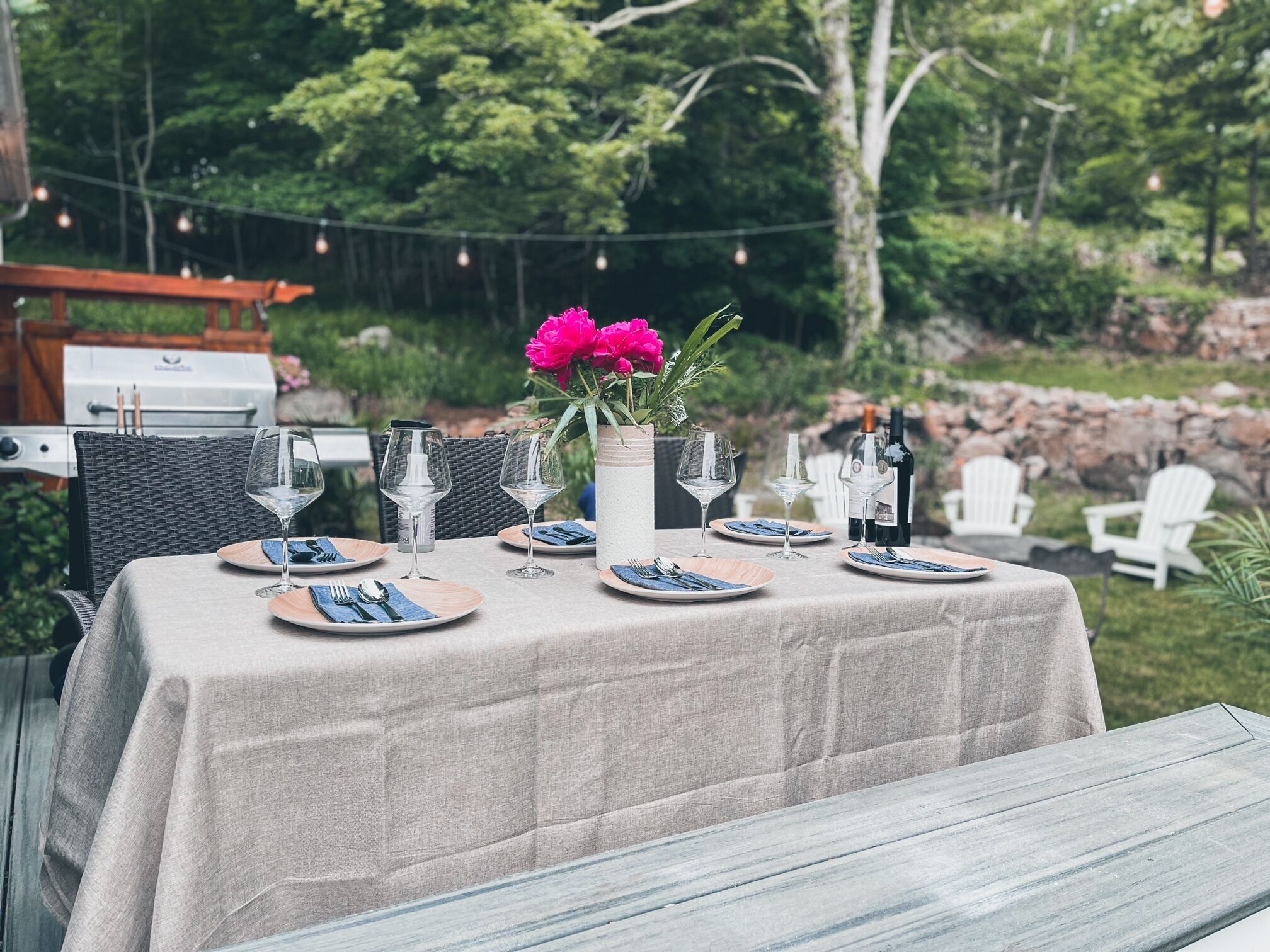 An outdoor dining area with a table set for four, surrounded by greenery and string lights.