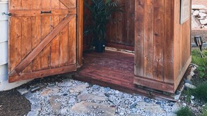 Une structure en bois dotée d’une grande porte, d’une petite fenêtre et d’un pot de fleurs suspendu.